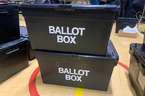 One black ballot box stacked on top of another ballot box at a vote count.