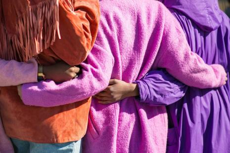 Backs of people with arms around each other with bright coloured coats on