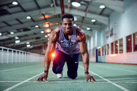 Gold medallist sprinter Harry Aikines-Aryeetey, on the starting line at an indoor racing track, smiling at the camera