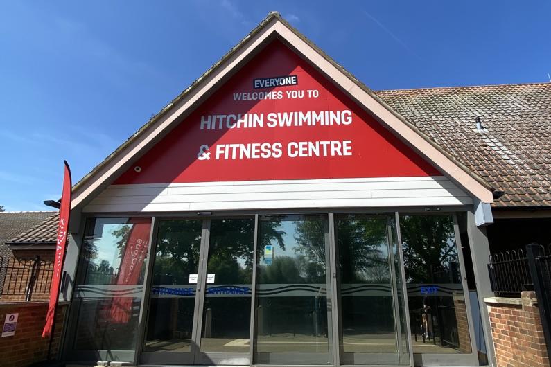 Entrance to Hitchin Swimming & Fitness Centre, with large red sign above glass doors.