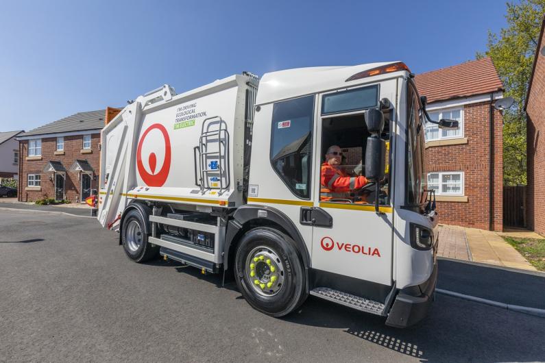 A Veolia electric waste vehicle being driven in a street with houses