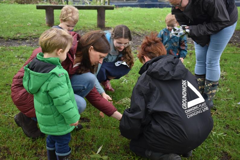 Groundwork officers kneeling down with children outside looking at things in the grass