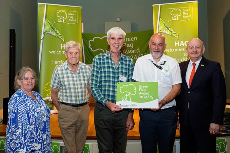 Two representatives from Friends of Norton Common with Council Service Manager Andrew Mills and two representatives from Keep Britain Tidy - holding a cardboard Green Flag in front of Green Flag signage